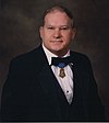 Portrait of a white man wearing a tuxedo with bow tie and a medal hanging from a blue ribbon around his neck