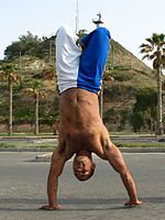 Capoeirista izvaja stojo na rokah s pokrčenimi nogami.