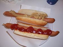 Doi hot-dog cu condimente.