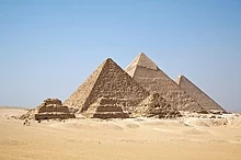 Una vista delle piramidi di Giza dall'altopiano a sud del complesso. Da destra a sinistra si trovano la Grande Piramide di Khufu, la Piramide di Khafre e la Piramide di Menkaure. Le tre piramidi più piccole in primo piano sono associate alla piramide di Menkaure.