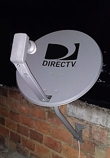 Eine Standard-DirecTV-Satellitenschüssel mit Dual-LNB an einer Ziegelwand. Die abgebildete Schüssel verwendet das alte Logo der genannten AT&amp;T-Tochtergesellschaft.