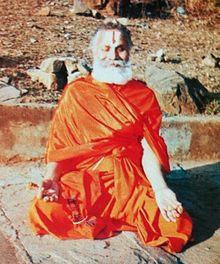 Rāmabhadrācārya bir Payovrata sırasında zihnini Mandakini nehrinin kenarlarında sabit tutuyor. Parmakları Çene Mudrası'nda katlanmış halde Sukhasana duruşunda.