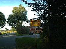 北ドイツの道路標識で、Elmlichheimはドイツ語名、Emelkapは低サクソン語名である。Elmlichheimはオランダとの国境で、ドイツ側にある。
