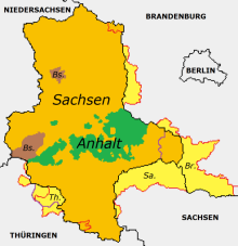 The borders of the GDR state of Saxony-Anhalt from 1947 to 1952 are shown in red, the outer borders of the GDR districts of Halle and Magdeburg in purple, and the current borders of Saxony-Anhalt in black. The part of Prussian Province Saxony is marked in yellow, the part of Anhalt in green, former Brunswick areas in brown.