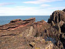 Siccar Point, Berwickshire. Engebeli nokta, 425 milyon yıllık Silüryen gri taşının dikey yataklarının üzerinde 345 milyon yıllık Devoniyen Eski Kırmızı Kumtaşı'nın hafif eğimli yataklarını göstermektedir.