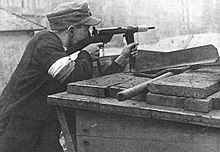 En af Armia Krajowa-soldaterne forsvarer en barrikade i Powiśle-distriktet under Warszawa-opstanden. Manden er bevæbnet med en Błyskawica-maskinpistol.