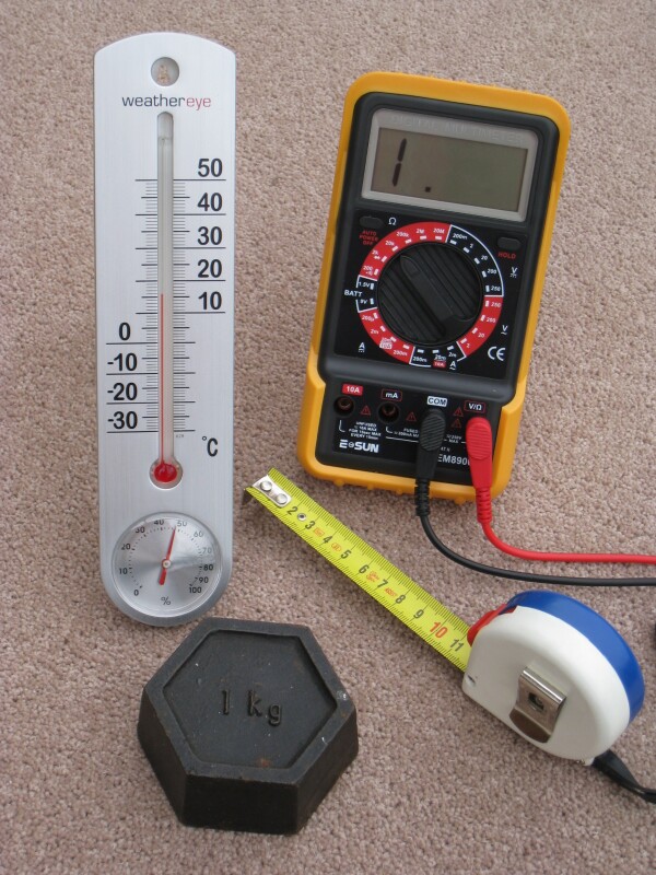 Štyri každodenné meracie prístroje s metrickou kalibráciou: meter kalibrovaný v centimetroch, teplomer kalibrovaný v stupňoch Celzia, kilogramové závažie a elektrický multimeter, ktorý meria volty, ampéry a ohmy.