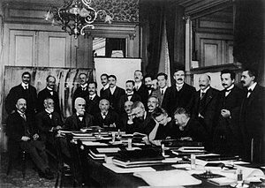 Conferința Solway 1911. Planck, Einstein și Jeans sunt în picioare. Planck este al doilea din stânga. Einstein este al doilea din dreapta. Jeans este al cincilea din dreapta. Wien este așezat, al treilea din dreapta.  