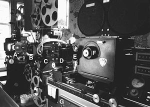 Imprimantă optică cu două capete de proiecție, utilizată la producerea de efecte speciale în filme. Pornind din stânga, se poate vedea lumina care strălucește de la casa lămpii, apoi la A se află poarta de film a primului proiector, la B o lentilă care proiectează filmul din A pe poarta celui de-al doilea proiector C. La D se află obiectivul camerei, vizorul camerei se află la E, iar la F comanda reglabilă a obturatorului. În baza grea G se află toate componentele electronice necesare pentru controlul imprimantei.