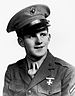 Head and shoulders of a young white man wearing a military jacket with a single cross-shaped pin on the left breast, one stripe on the upper sleeve, and a peaked cap with an eagle-globe-and-anchor emblem on the front.