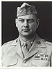 Head and shoulders of a middle-aged white man with a round face wearing a garrison cap and a jacket with four rows of ribbon bars on the left breast and pins on both the lapels and on the collar of the undershirt.