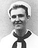 Head and shoulders of a smiling young white man wearing a naval uniform consisting of a white shirt with a dark scarf tied around the neck and running under the large, flat, collar, and a white "Dixie Cup" hat.