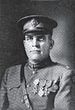 Head and shoulders of a middle-aged man in military uniform with a strap across his chest, four medals on his left breast, and a peaked cap.