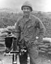 A black and white image showing Hector from the waist up in his military combat uniform with kevlar helmet. His hands are on his hips and he is smiling at the camera.