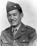 Head and shoulders of a smiling young man wearing a garrison cap and a military jacket with chevrons on the upper sleeve over a shirt and tie