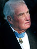 Head of an older white man with gray hair wearing a dark suit coat over a white shirt. A star-shaped medal hangs from a light-blue ribbon around his neck.