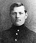 Head of a young man with thick, dark, hair parted at the side. He is wearing a military jacket with a high collar and bright buttons down the center.
