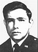 Head of a young white man with thick hair wearing a dark military jacket with a "U.S." pin on the lapel.