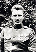 Head and shoulders of a man in military uniform with combed back hair and a neatly trimmed mustache. Three medals hang from ribbons on his chest.