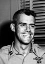 A head and shoulders portrait of a young, cleanshaven man with dark hair, wearing a military uniform. He is smiling broadly.