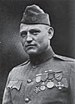 Head and shoulders of a man in a neatly-pressed military uniform with four medals hanging from ribbons on his chest and a garrison cap.