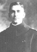 Head and shoulders of a young white man with a cleft chin and neatly combed hair parted at the side. He is wearing a dark, heavy, pea coat with military shoulder straps.