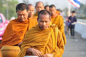 Thaimaalaiset buddhalaismunkit kävelevät varhain aamulla keräämään almuja.