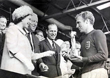 Królowa wręcza Puchar Świata w 1966 r. Bobby'emu Moore'owi, kapitanowi zwycięskiej drużyny Anglii. Mecz został rozegrany pomiędzy Anglią a Niemcami Zachodnimi 30 lipca 1966 r. na stadionie Wembley. Anglia wygrała 4-2 po dogrywce.