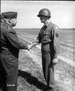 Two white men in military dress uniform shaking hands. One is an Older man and on is a young man.